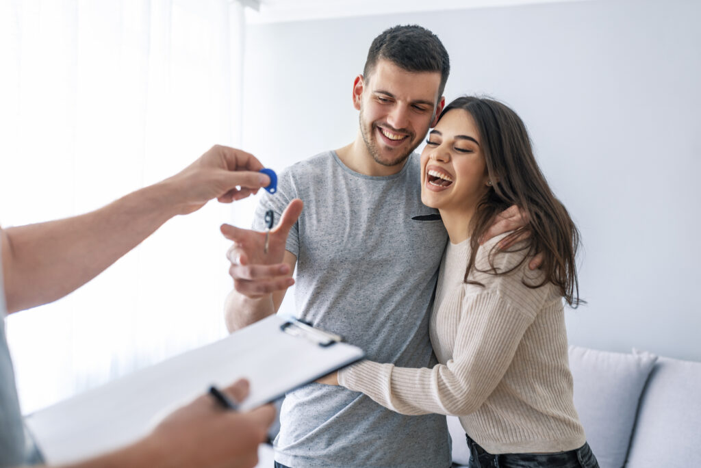 Happy couple is taking keys from their new house from broker and smiling.